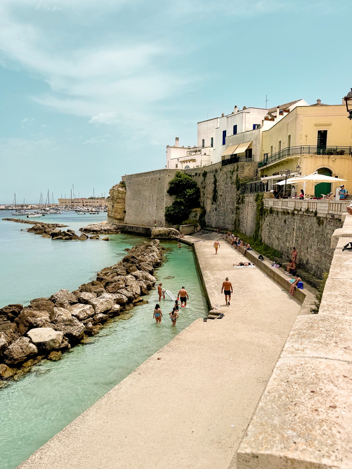 Ultimate Puglia Vacation Guide: Locals sunbathing and enjoying the clear water at Via dei Bastioni Beach in Otranto, Puglia, Italy