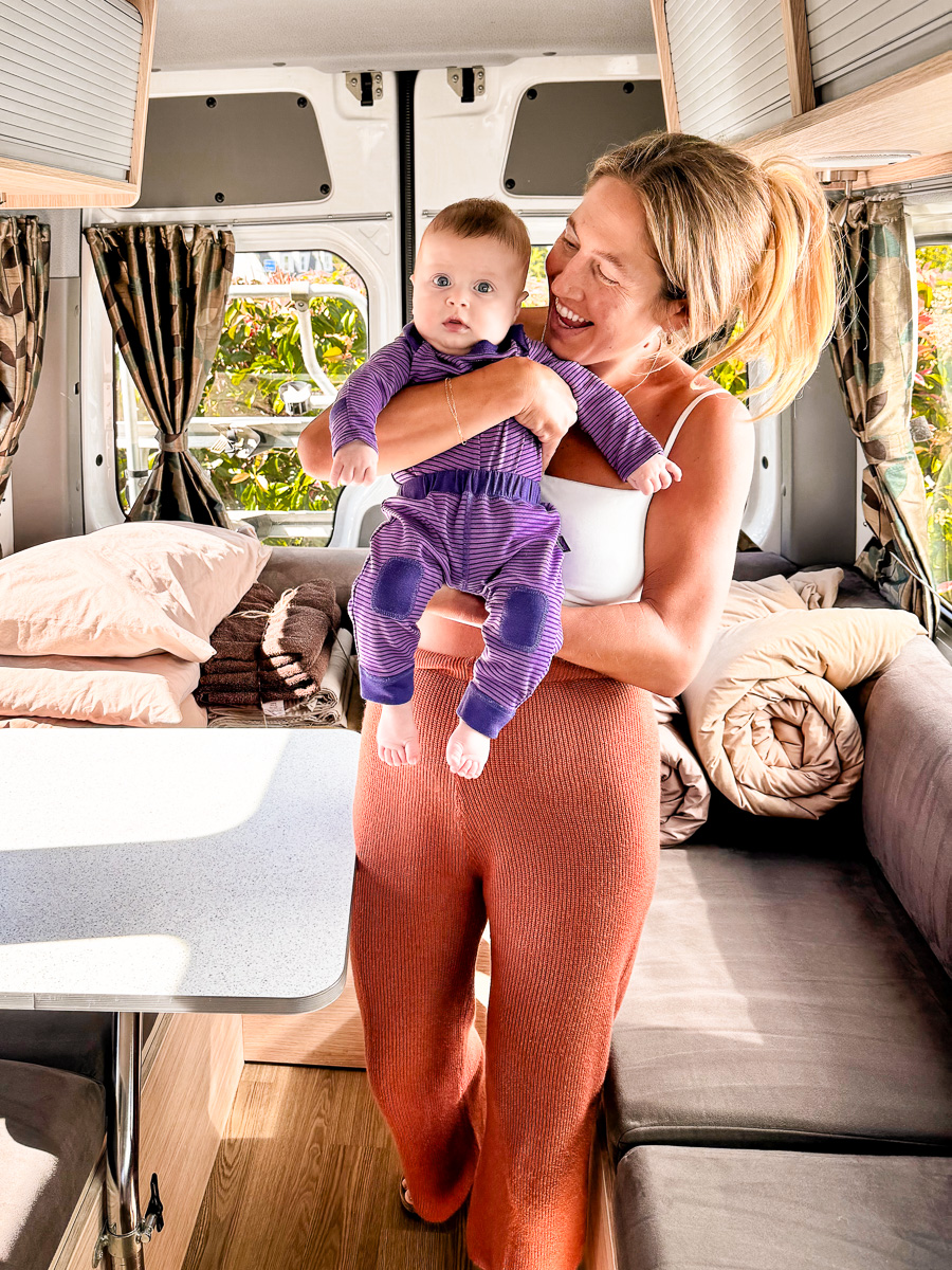 Mom holding Infant inside a Campervan at the beginning of a trip renting a campervan in New Zealand with an infant.