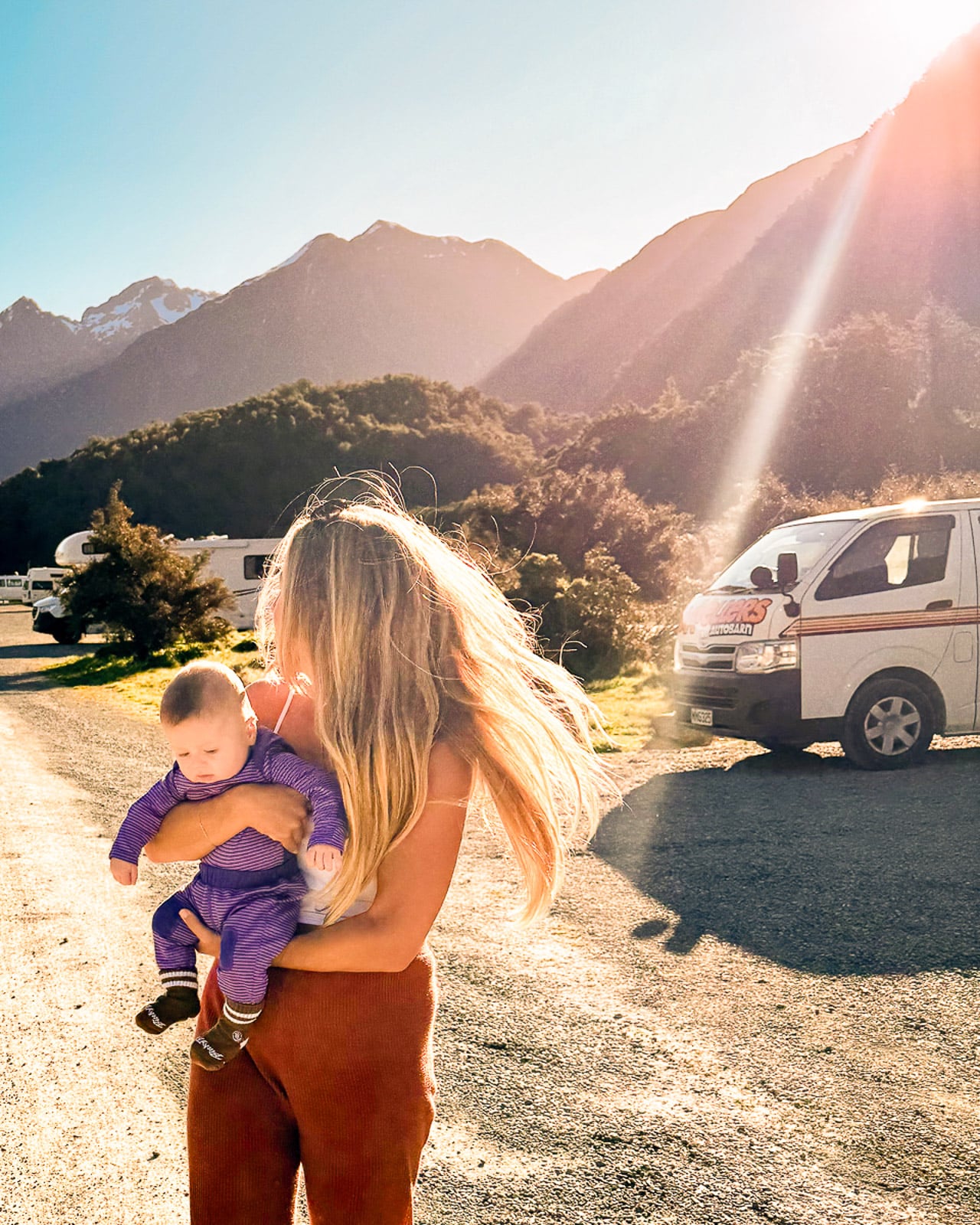 Mom holding an infant in front of a campervan at a camp site near Mildford Sound, New Zealand