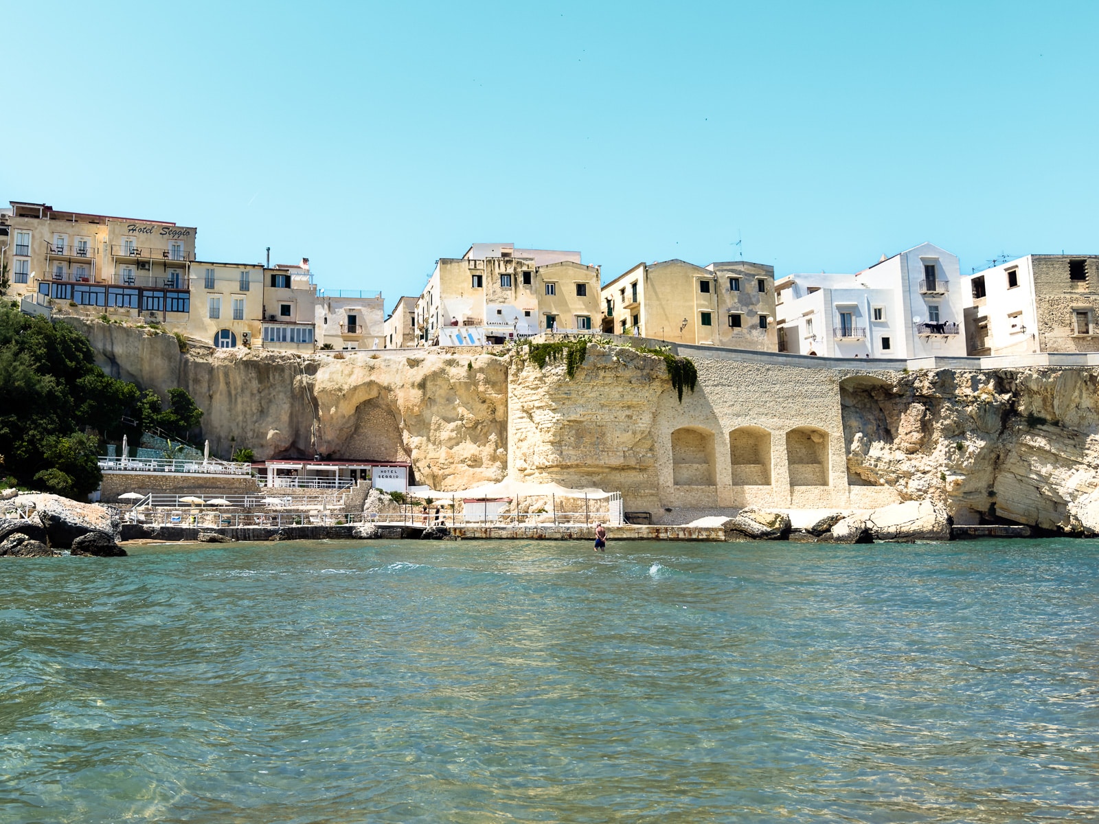 Ultimate Puglia Vacation Guide: View from the water of the Hidden beach near Hotel Seggio and the limestone cliff walls of the town in Vieste, Puglia, Italy 