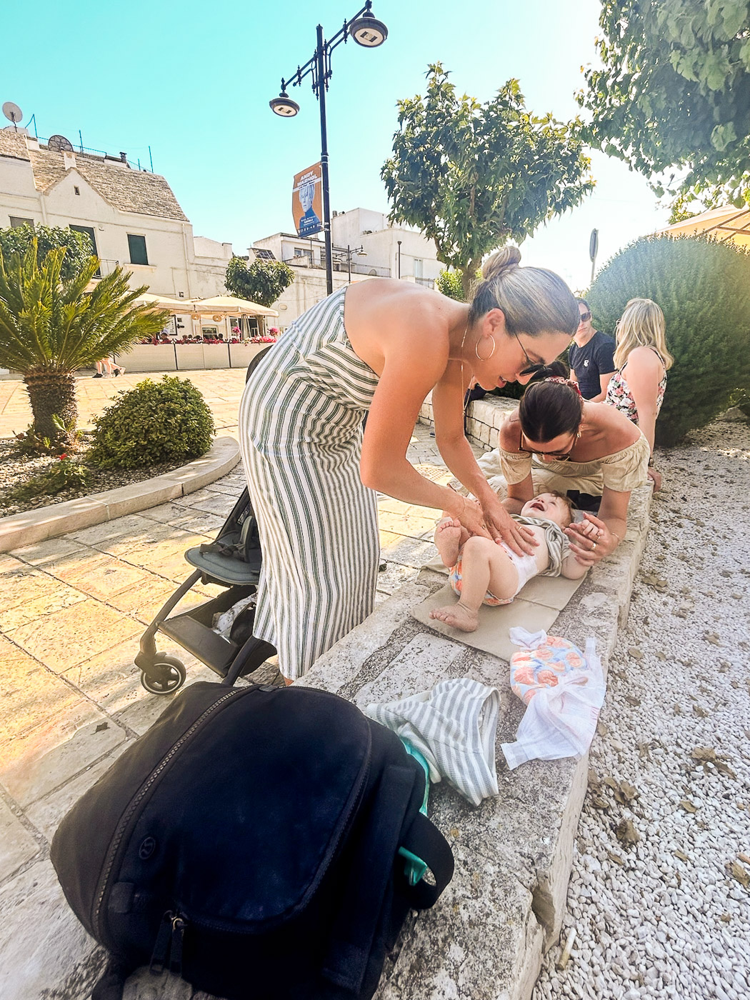 Essential Packing List for Traveling to Europe with a Baby: Mom changing baby on bench outside in Alberobello, Puglia, Italy