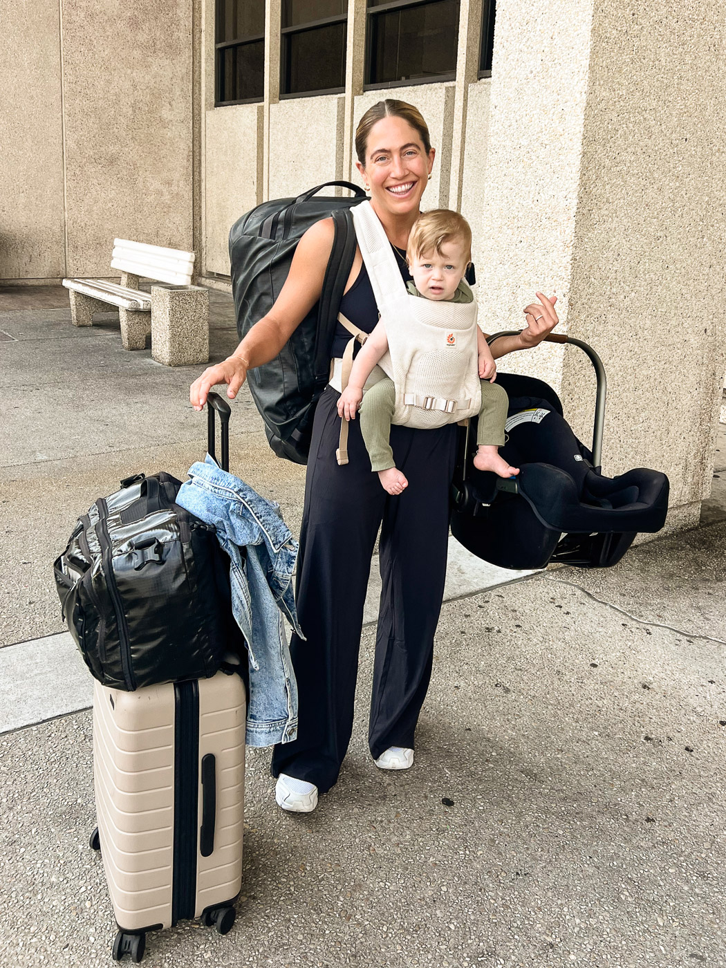 Essential Packing List for Traveling to Europe with a Baby: Mom outside Airport With Luggage While Wearing Baby in a Baby Carrier