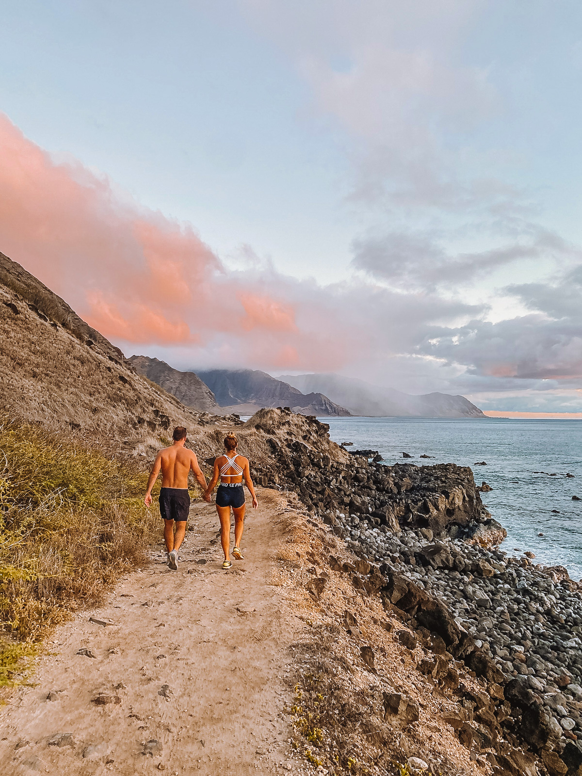 Best Spots for Whale Watching in Oahu Blog Post Picture: Man and Woman walking along the trail to Kaena Point on the West Side of Oahu, Hawaii with the mountains of Hawaii and the Pacific Ocean in the background.