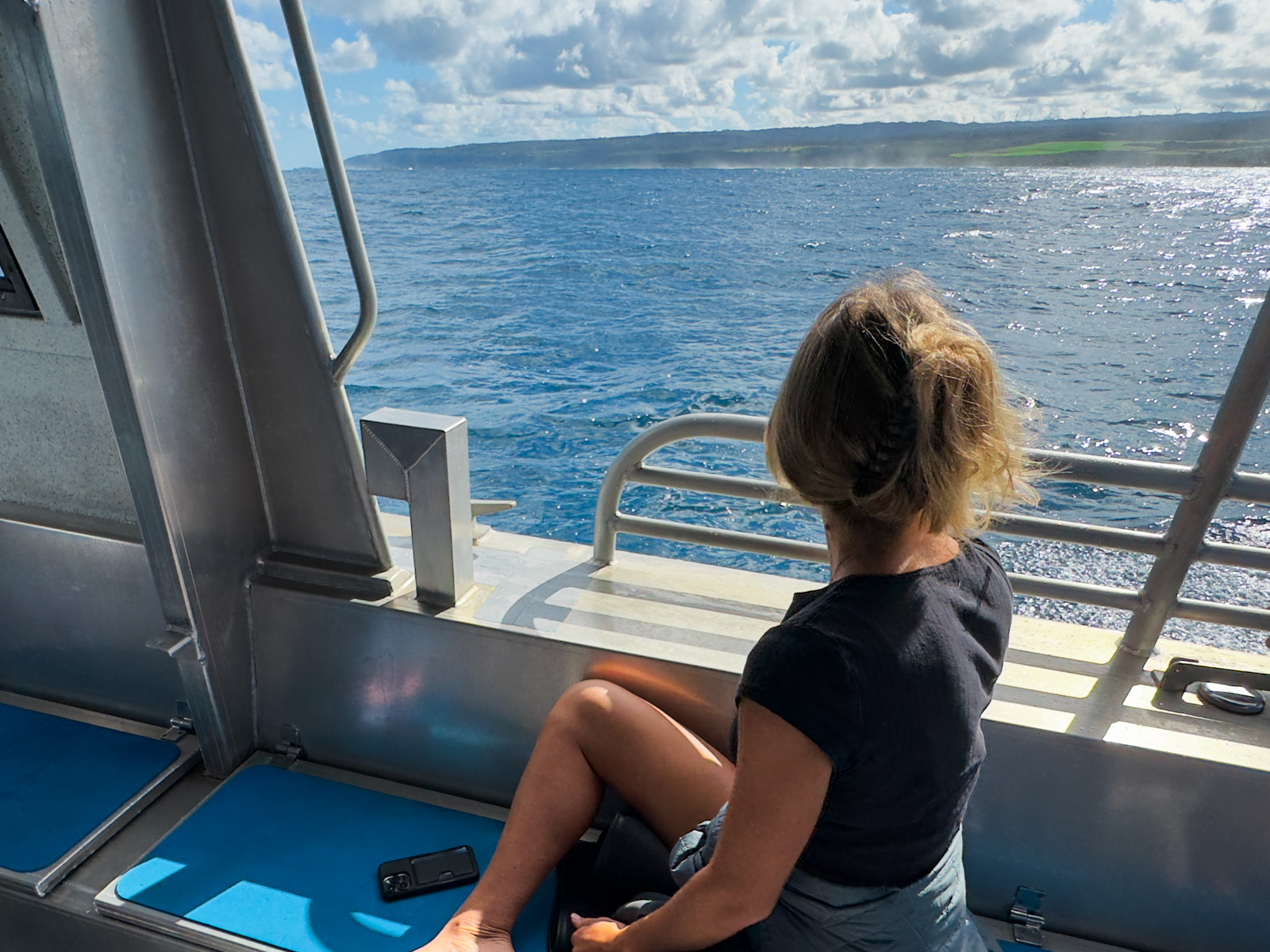 Best Whale Watching Spots on Oahu Blog Photo: Woman sitting on a shark-watching boat in Haleiwa, North Shore, Oahu, gazing out over the blue ocean with the coastline visible in the distance under a partly cloudy sky.