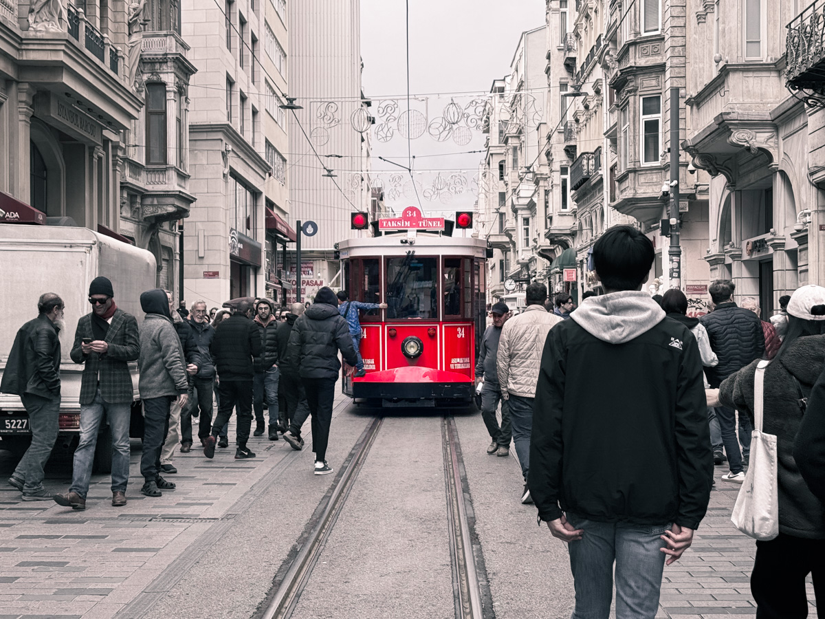 11 Best, Most Unique Things to Do in Istanbul, Turkey: A historic red tram travels down the bustling Istiklal Street in Istanbul, Turkey, surrounded by crowds of pedestrians walking along the tracks and past ornate European-style buildings.